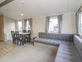 Ein modernes Wohnzimmer mit einem grauen Ecksofa, einem Esstisch mit Stühlen und einem Fenster mit karierten Vorhängen.