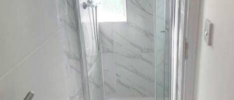 Ducha con cerramiento de vidrio, suelo de mármol y una ventana pequeña.