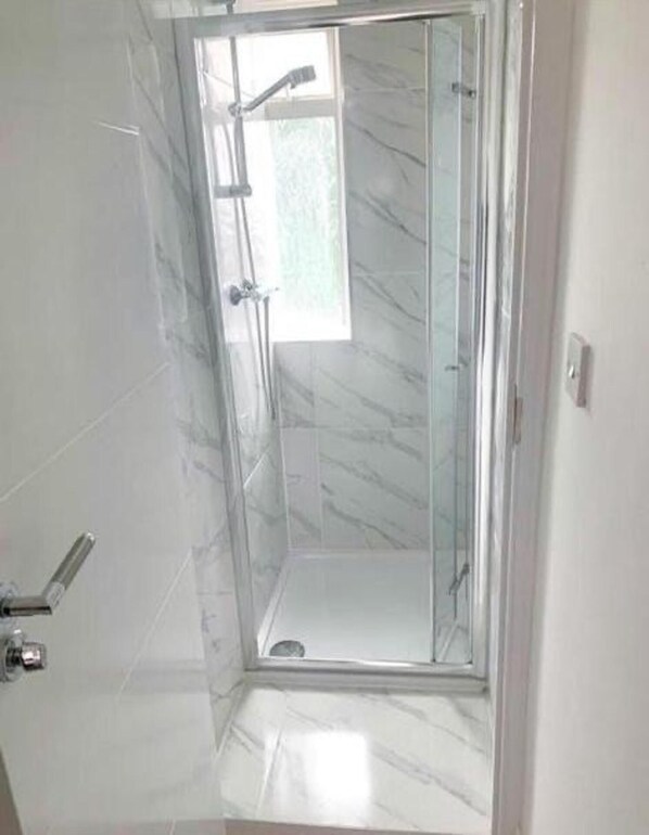 Eine begehbare Dusche mit Glaswänden, einem Marmorboden und einem kleinen Fenster.