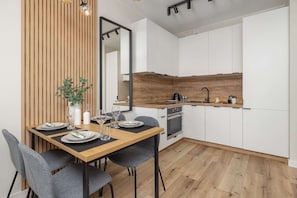 A modern kitchen with white cabinets, a wooden countertop, and a dining area with a table set for two.