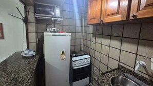 Een kleine keuken met een koelkast, magnetron, fornuis en spoelbak.