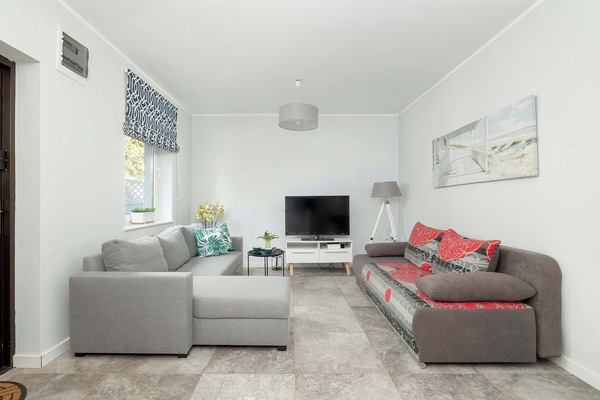 A bright studio, with a window letting natural light in, with a sofa and corner sofa and TV.