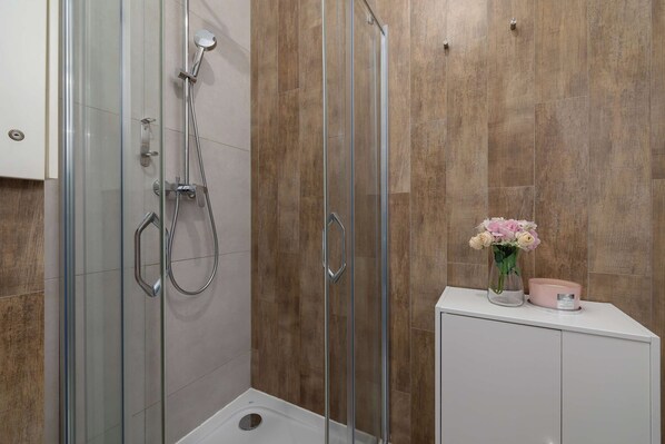 A glass-enclosed shower cabin stands in a contemporary bathroom. The interior walls of the shower are lined with textured, wood-look tiles.