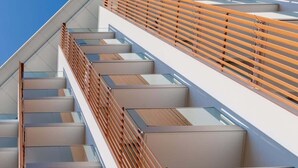 A modern staircase with glass railings and wooden steps, leading to a second-floor balcony.