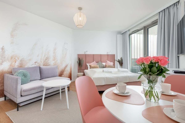 A cozy bedroom featuring a double bed with a pink upholstered headboard and soft bedding, complemented by bedside tables and decor.