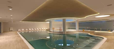 A modern indoor pool with a central column, lounge chairs, and a unique ceiling design.