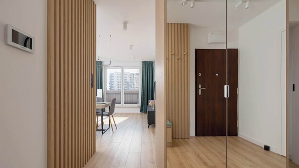 A modern interior with a wooden floor, a dining area with a table and chairs, and a large wooden wardrobe.