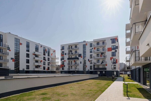 Un moderno complejo de apartamentos con varios balcones, un camino pavimentado y una zona ajardinada.