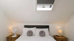 A neatly made bed with two pillows and a headboard, a bedside table with a lamp, and a small window with a view of the sky. - Barn Cottage (Frome)