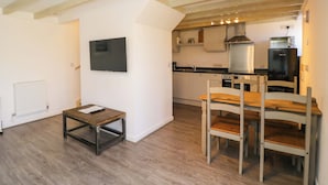 A modern kitchen with wooden beams, a flat-screen TV, and a dining area with a table and chairs. - Barn Cottage (Frome)