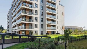A multi-story residential building with balconies, a flat roof, and a grassy area in front.