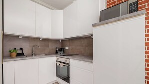 A compact kitchen with white cabinets, a built-in oven, a sink, and a microwave.