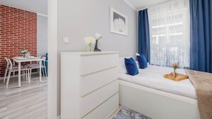 A modern room with a white bed, blue curtains, a white dresser, and a dining area with a white table and chairs.