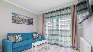 A modern living room with a blue sofa, a white coffee table, and a cityscape painting on the wall.