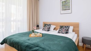 Ein ordentlich bezogenes Bett mit einem grünen Überwurf, zwei Kissen mit Blättermotiv und einem Tablett mit Tassen und einer Blume.