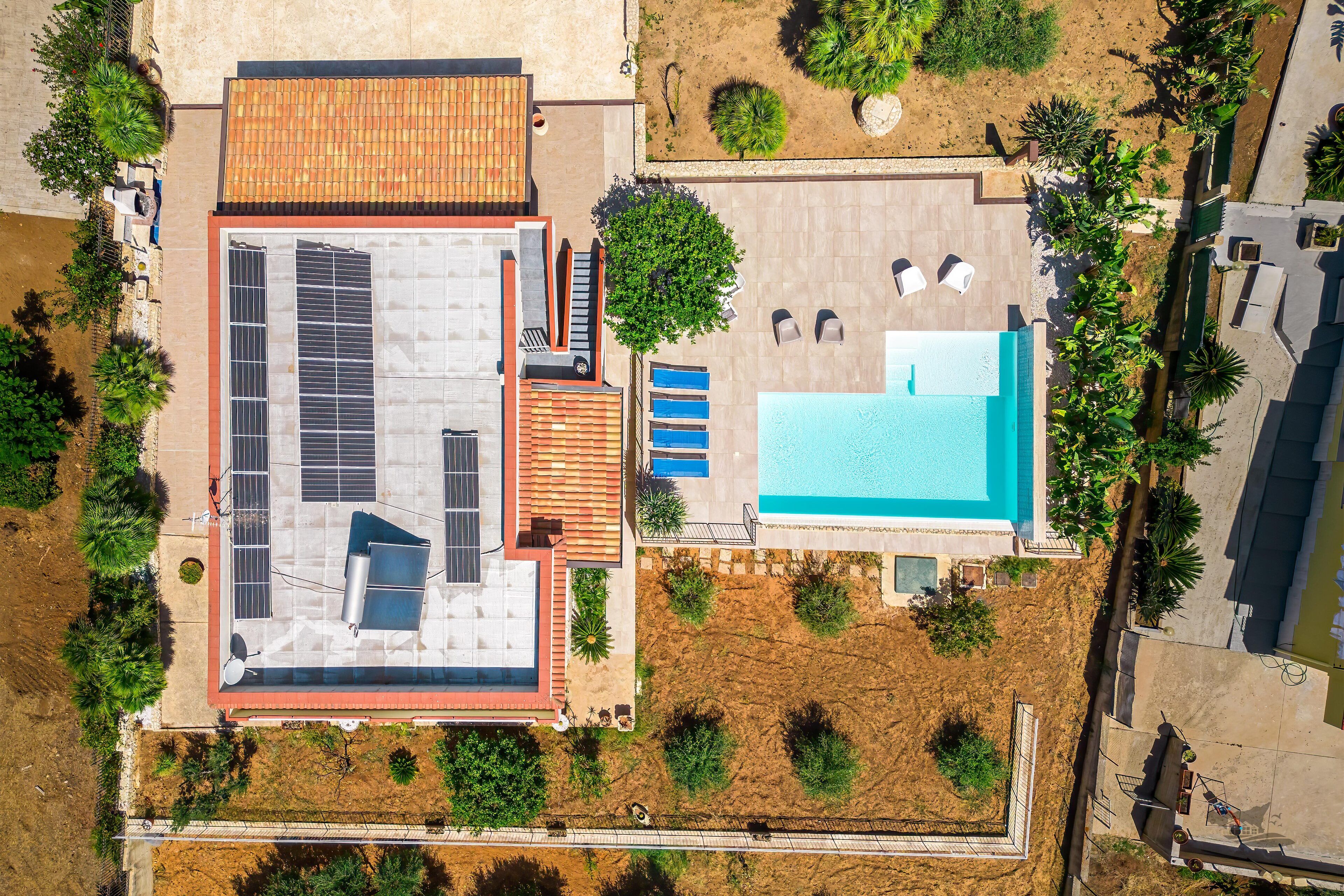 An aerial view of a building with a swimming pool, solar panels, and a patio area with seating.
