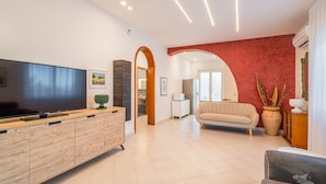 A modern living room with a flat-screen TV, wooden entertainment unit, and a beige sofa. - Villa DellAcqua: Infinity Pool with Sea View (Alcamo)