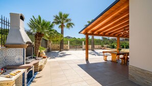 An outdoor patio with a stone barbecue, wooden pergola, and seating area. - Villa DellAcqua: Infinity Pool with Sea View (Alcamo)