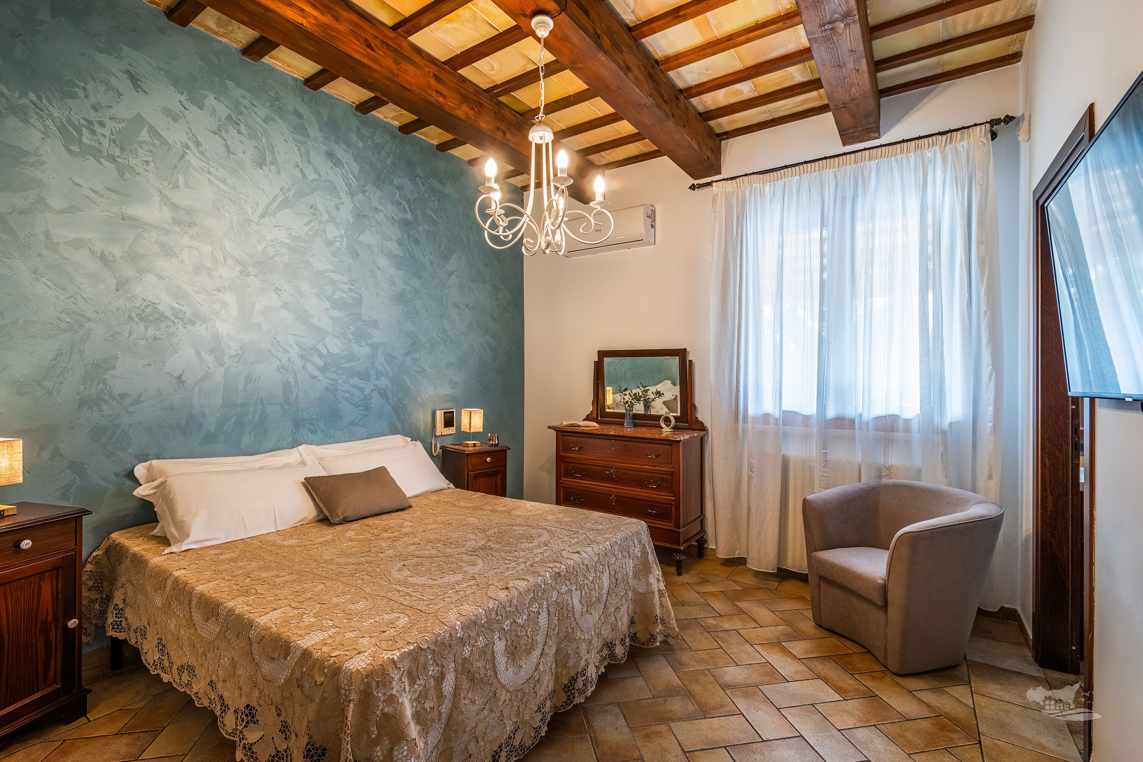 Ein Schlafzimmer mit Bett, Schminktisch, Sessel, Fernseher und einer Deckenleuchte.