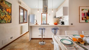 A modern kitchen with two bar stools, a dining table set for two, and a large window. - Villa DellAlbero: Privacy, Relax and Unique Pool (Alcamo)
