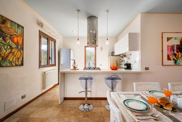 Una cocina moderna con dos taburetes de bar, una mesa de comedor para dos personas y un amplio ventanal.
