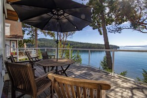 A wooden deck with a table and chairs, overlooking a lake with trees and hills in the background.