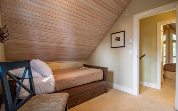 Un dormitorio con techo inclinado, una cama, una silla y una mesita.