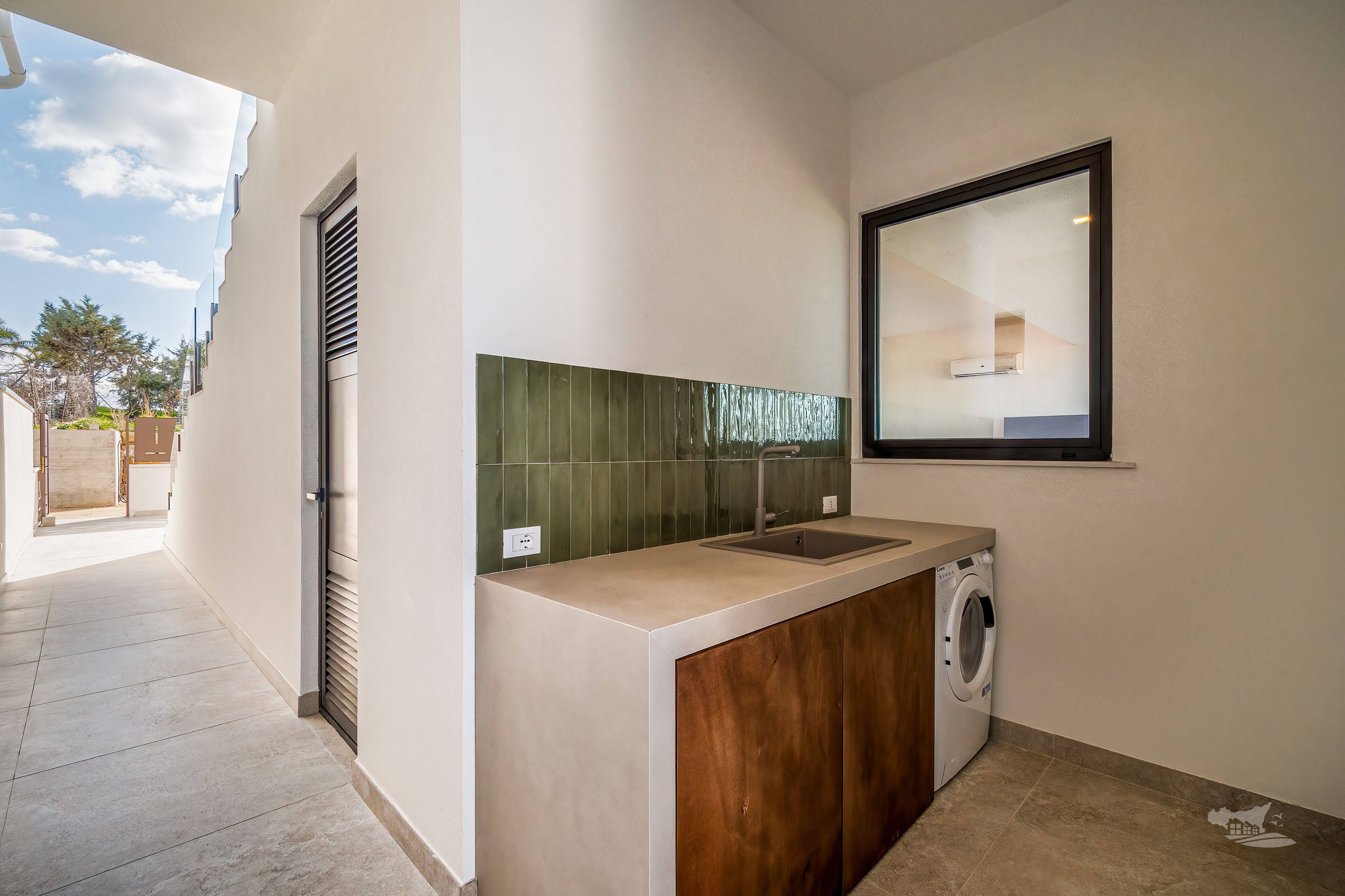 A compact kitchen with a built-in washing machine, a sink, and a window above the counter.