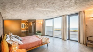 A modern hotel room with a large bed, a round mirror, a small table with a lamp, and a view of the sea through large windows. - Villa Brezza: Infinity Pool with Sea View (Partinico)