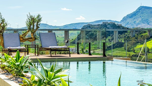 A pool area with lounge chairs and a view of a bridge and hills. - Villa Castello: Pool with Sea and Castle Views (Partinico)