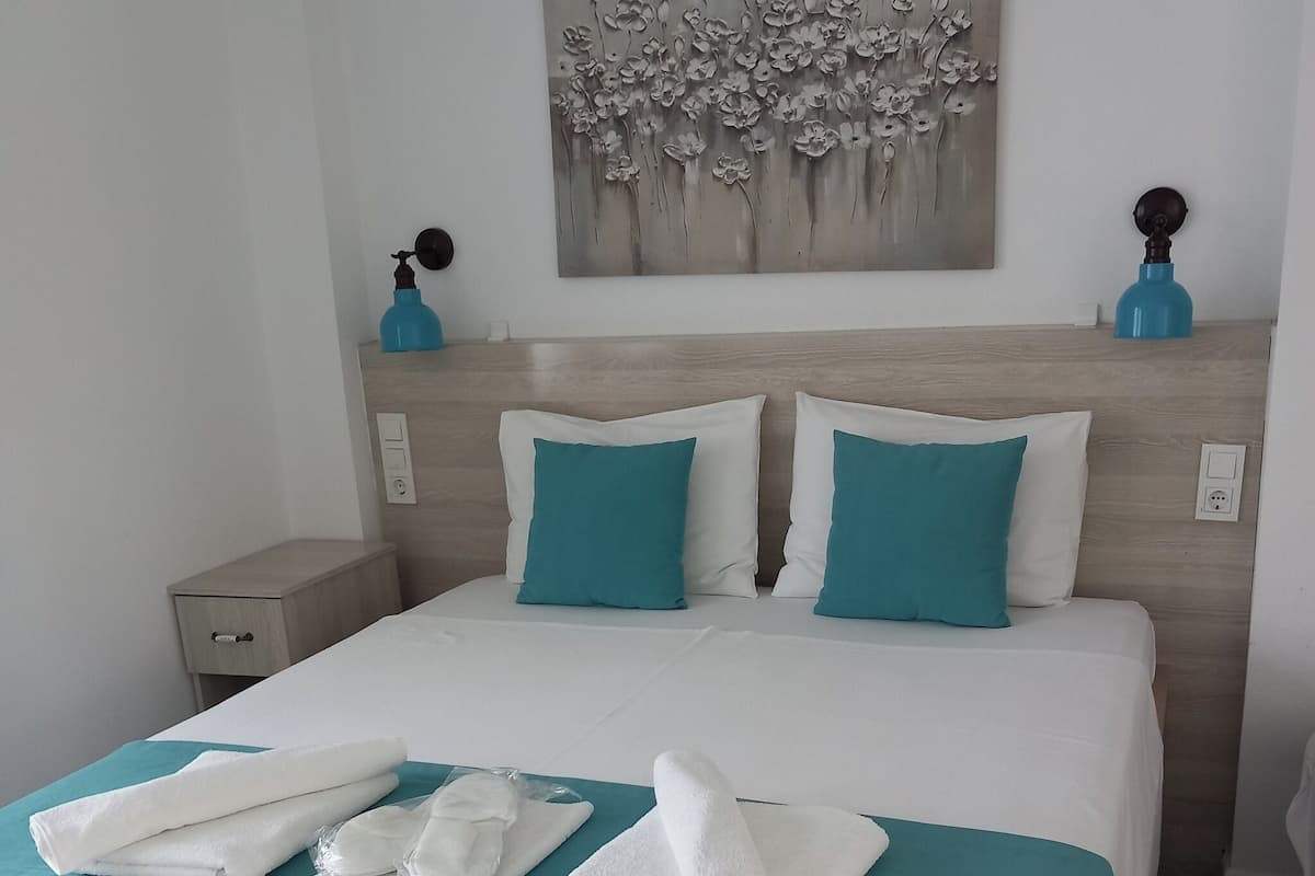 Un letto rifatto con cura, con biancheria bianca e azzurro mare, un quadro appeso sopra e un pavimento a motivi.