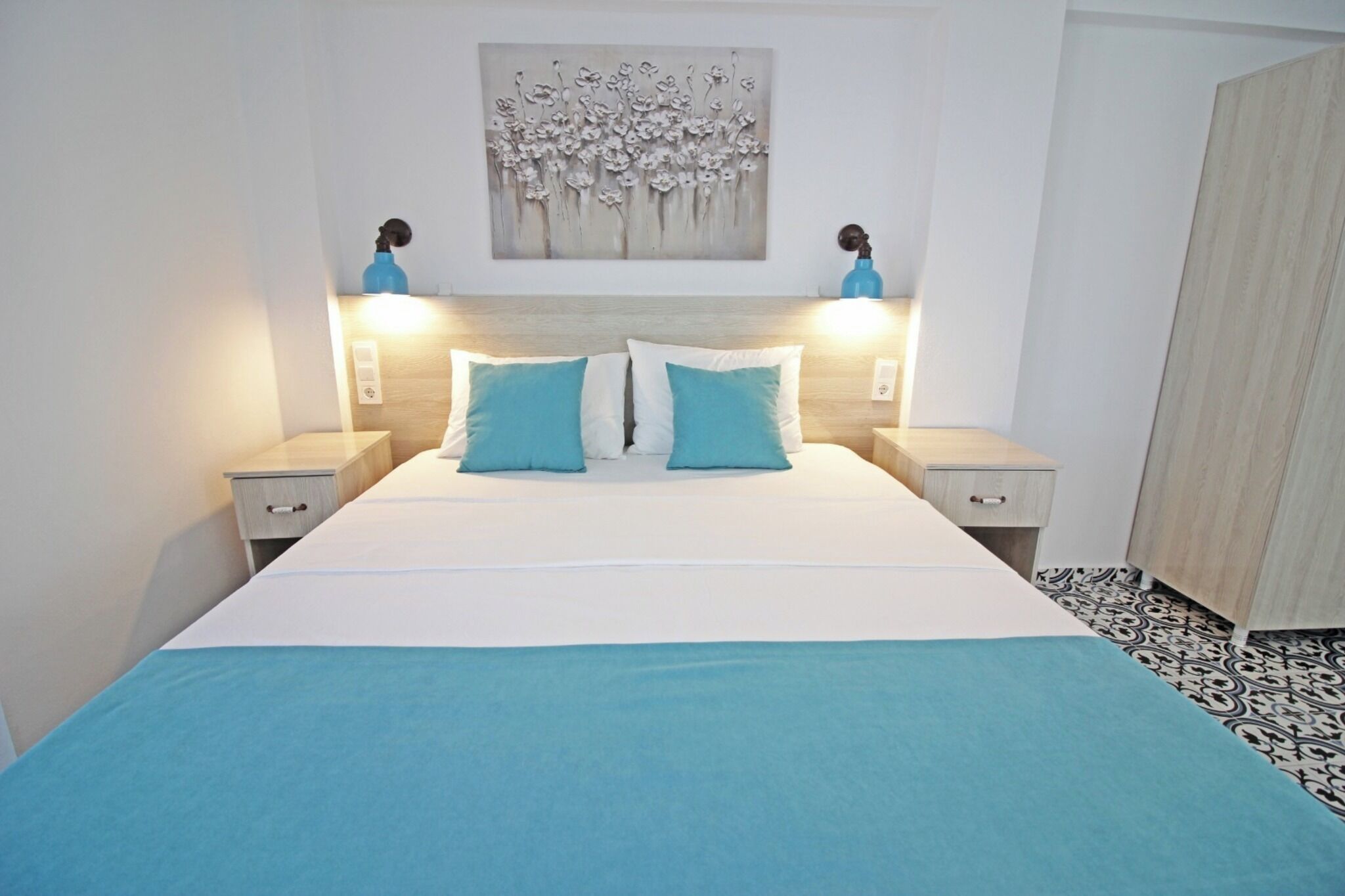 A bedroom with a bed, two bedside tables, a wall-mounted artwork, and a patterned floor.
