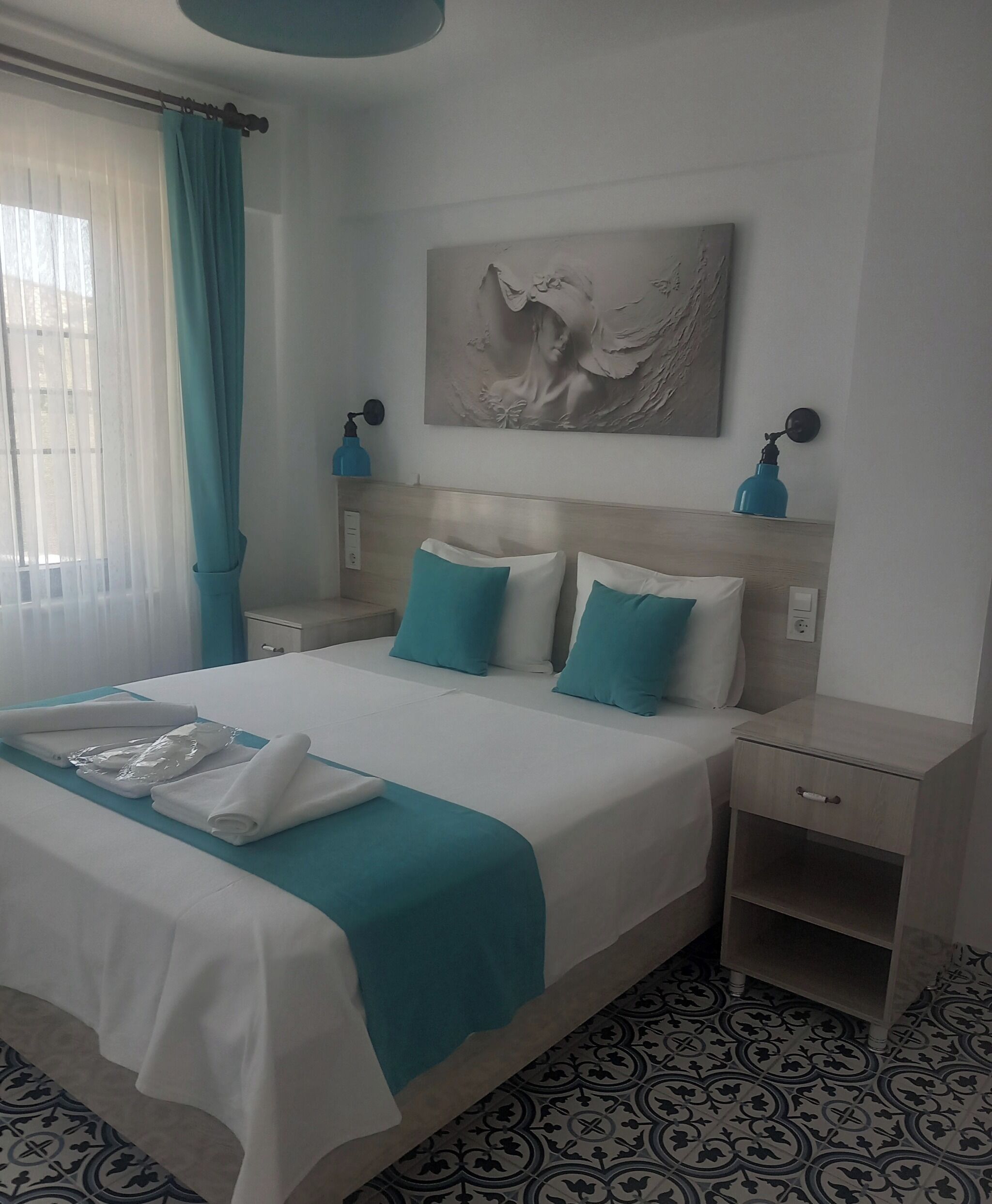 A hotel room with a bed, a nightstand, a wall-mounted lamp, and a painting.