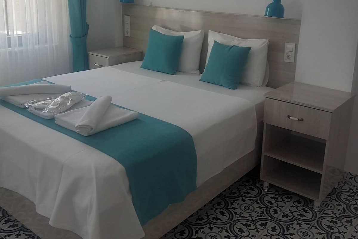 Una camera d'albergo con un letto, un comodino, una lampada a parete e un quadro.