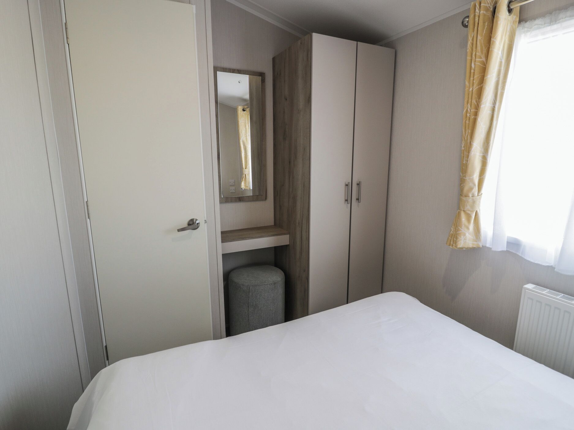 A bedroom with a bed, a wardrobe, a mirror, a radiator, and a window with curtains.