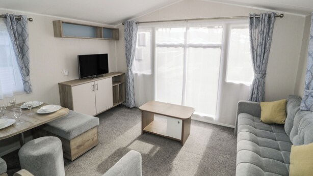 A compact living space with a sofa, a dining table with chairs, a TV, and a small kitchenette. - Lido Gold 273 (Prestatyn)