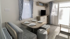 A compact living space with a dining area, a sofa, a TV, and a small kitchenette. - Lido Gold 273 (Prestatyn)
