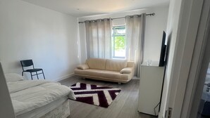 A modern bedroom with a bed, a sofa, a TV, and a window with curtains. - Sunny Gardens London House Retreat (London)