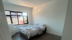 A bedroom with a bed, a dresser, and a window with blinds. - Sunny Gardens London House Retreat (London)