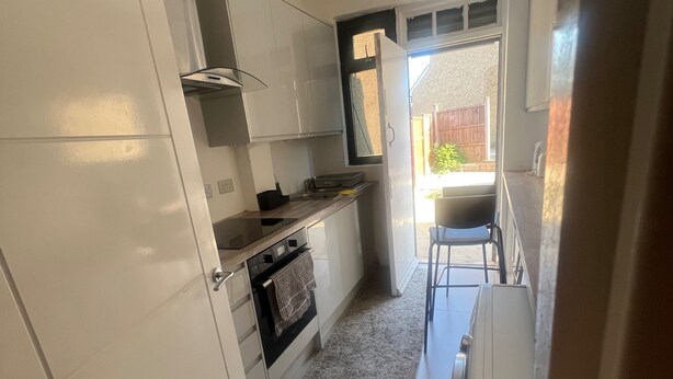 A compact kitchen with white cabinets, a built-in oven, and a small window. - Sunny Gardens London House Retreat (London)