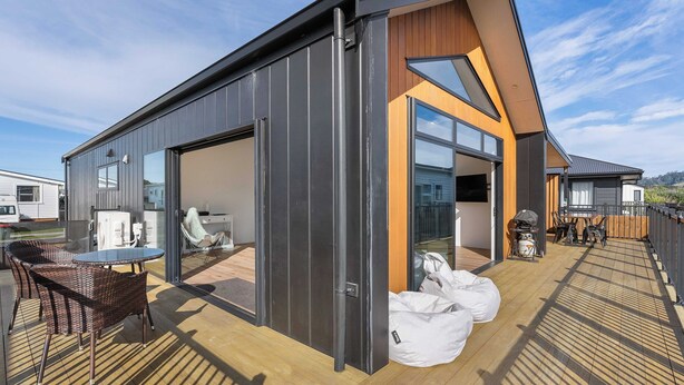 A modern building with a large glass door, outdoor seating area, and a wooden deck.