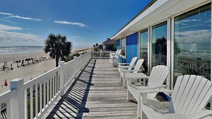 A wooden deck with white chairs and a railing overlooking a beach. - Bermuda Blue by Ryson Vacation Rentals (Galveston)