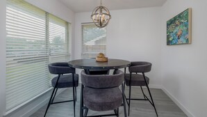 Een eetruimte met een ronde tafel, vier stoffeerde grijze stoelen, een hanglamp en een schilderij aan de muur.