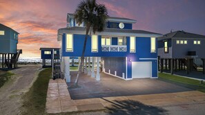 A coastal house with a two-story design, featuring a covered porch and a garage. - Captain's Manor by Ryson Vacation Rentals (Galveston)