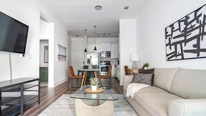 A modern living room with a glass coffee table, a beige sofa, and a dining area with chairs and a table. - Landing Weston Lakeside Apartments (Cary)