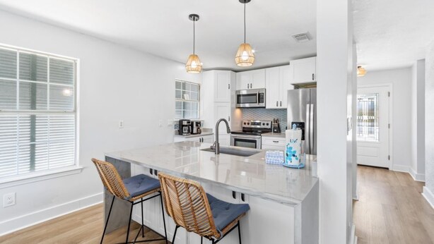 A modern kitchen with white cabinets, a central island with bar stools, and pendant lighting.