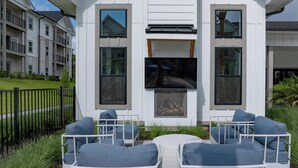 Un área de estar moderna al aire libre con una televisión de pantalla plana, sillas de metal blanco y una mesa pequeña.