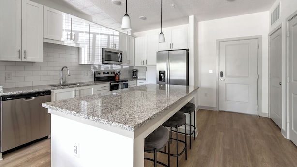 Una cocina moderna con armarios blancos, encimera de granito, electrodomésticos de acero inoxidable y una zona con taburete de bar.