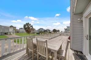 A wooden deck with a table and chairs, overlooking a residential area with houses and a clear sky. - Crab Claw by Ryson Vacation Rentals (Galveston)
