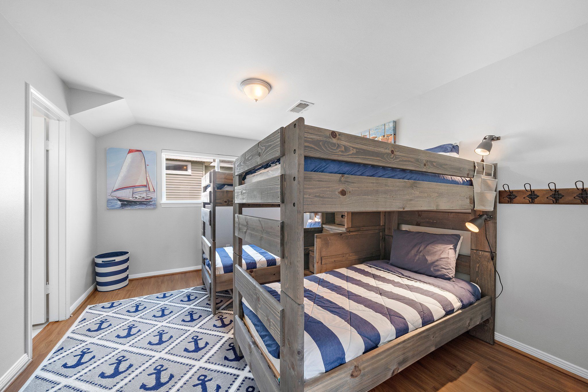 Uma cama beliche com estrutura de madeira, um edredom listrado e uma luminária de leitura fixada na parede.